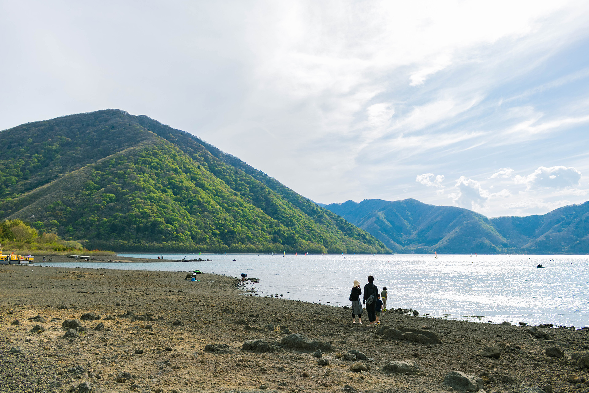 Edge of a lake with lush mountains in the background.